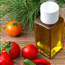 Ελαιόλαδο, φρέσκα λαχανικά, και βότανα ελληνικής αγροτικής παραγωγής, σε ένα τραπέζι υπό φως μεσογειακού ήλιου.